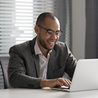 Smiling african american businessman in suit working on computer sit at office desk, happy mixed race worker entrepreneur typing email on laptop communicating online using software for business